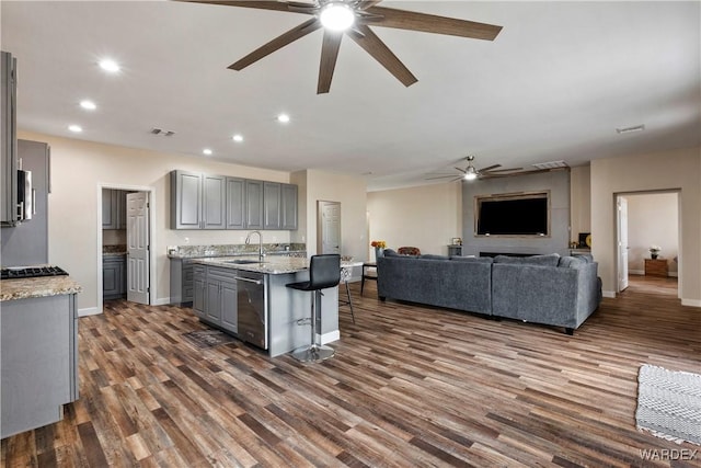 kitchen with gray cabinetry, a sink, open floor plan, stainless steel dishwasher, and a center island with sink