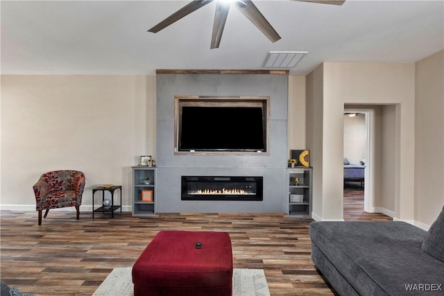 living area with a large fireplace, visible vents, baseboards, and wood finished floors