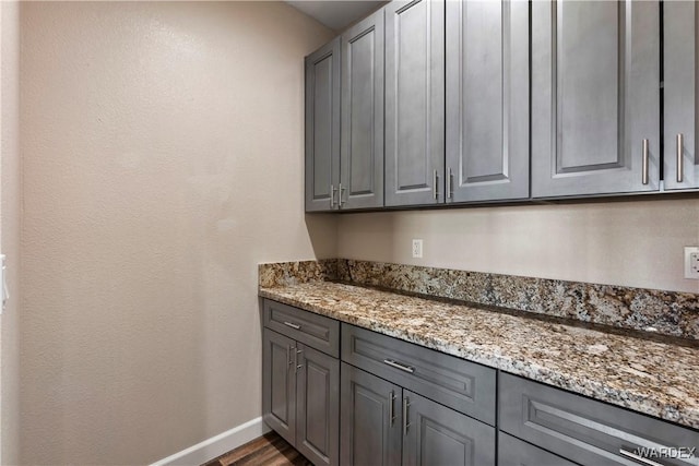 kitchen with dark wood-style floors, baseboards, light stone counters, and gray cabinets