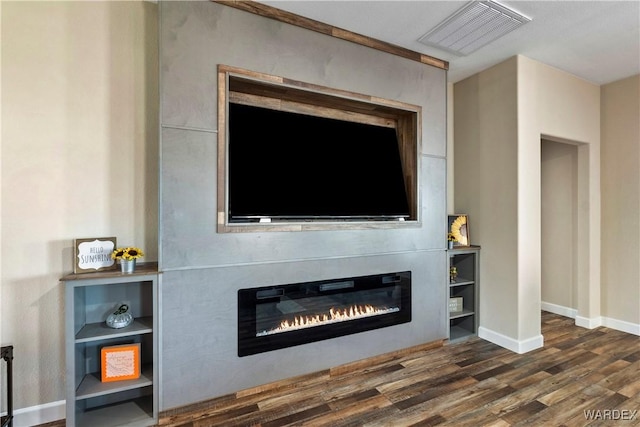 interior details with wood finished floors, a glass covered fireplace, visible vents, and baseboards