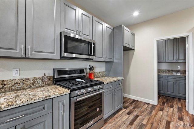 kitchen featuring light stone counters, gray cabinetry, dark wood-type flooring, baseboards, and appliances with stainless steel finishes