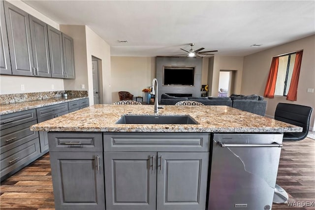 kitchen with stainless steel dishwasher, open floor plan, a sink, and gray cabinetry