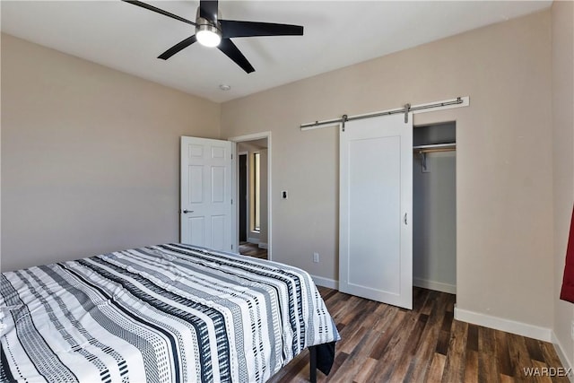 bedroom featuring a barn door, baseboards, a ceiling fan, dark wood-style flooring, and a closet