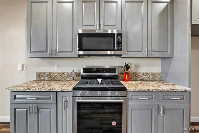 kitchen featuring stainless steel appliances, baseboards, gray cabinetry, and light stone countertops