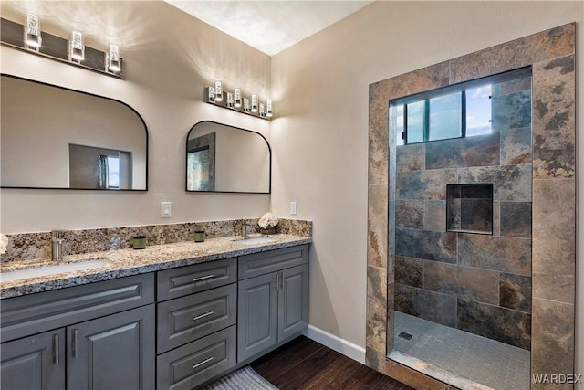 full bathroom featuring double vanity, a walk in shower, a sink, and wood finished floors