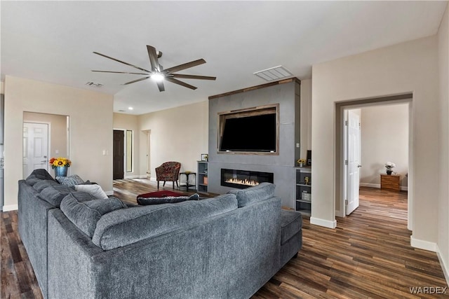 living room with a large fireplace, baseboards, visible vents, dark wood finished floors, and ceiling fan