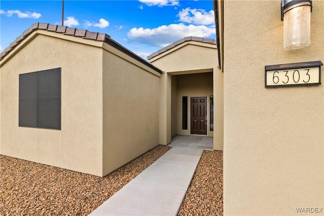 doorway to property featuring a tile roof and stucco siding