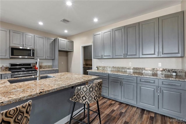 kitchen with dark wood finished floors, stainless steel appliances, visible vents, gray cabinetry, and light stone countertops