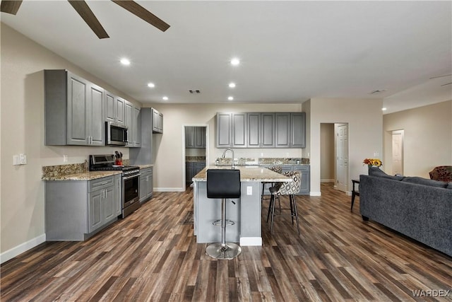 kitchen with light stone counters, stainless steel appliances, gray cabinetry, an island with sink, and a kitchen bar