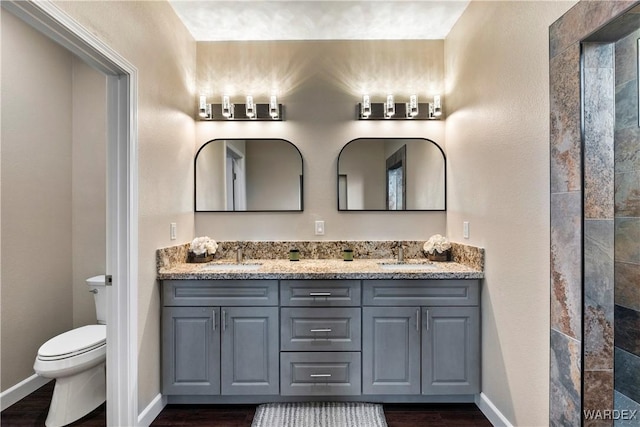 bathroom featuring toilet, double vanity, baseboards, and a sink