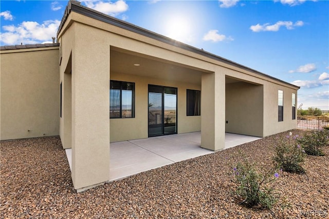 rear view of house featuring a patio area, fence, and stucco siding