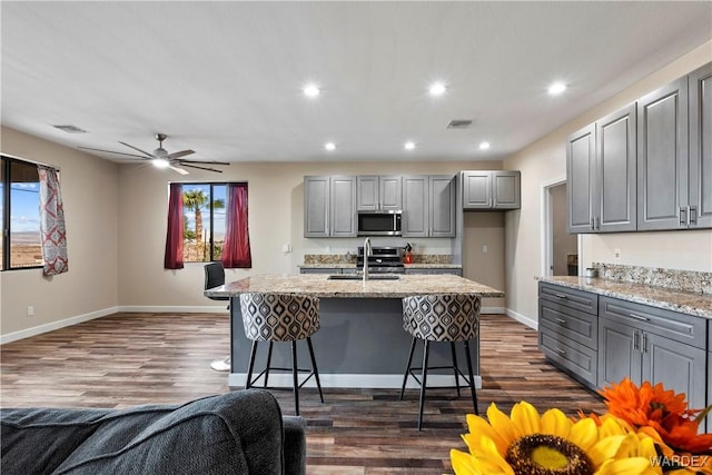 kitchen featuring a kitchen island with sink, a sink, visible vents, gray cabinets, and stainless steel microwave