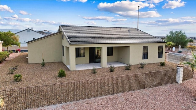 rear view of property featuring a tiled roof, a patio, fence, and stucco siding