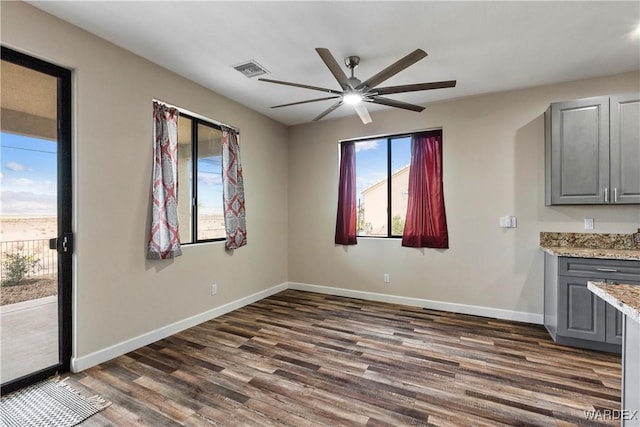 unfurnished living room with a ceiling fan, visible vents, baseboards, and dark wood-type flooring