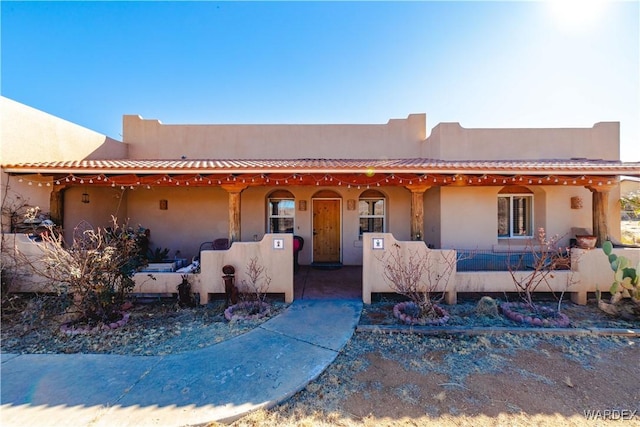 adobe home with a tiled roof, a porch, and stucco siding