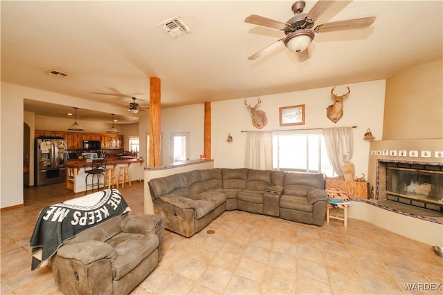 living room featuring a glass covered fireplace, visible vents, and ceiling fan