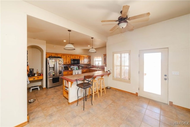 kitchen with black microwave, a breakfast bar area, a peninsula, stainless steel fridge with ice dispenser, and pendant lighting