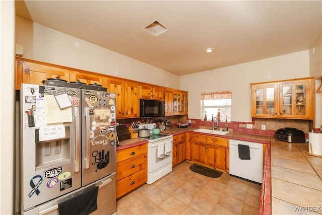 kitchen featuring white appliances, tile counters, brown cabinetry, glass insert cabinets, and a sink