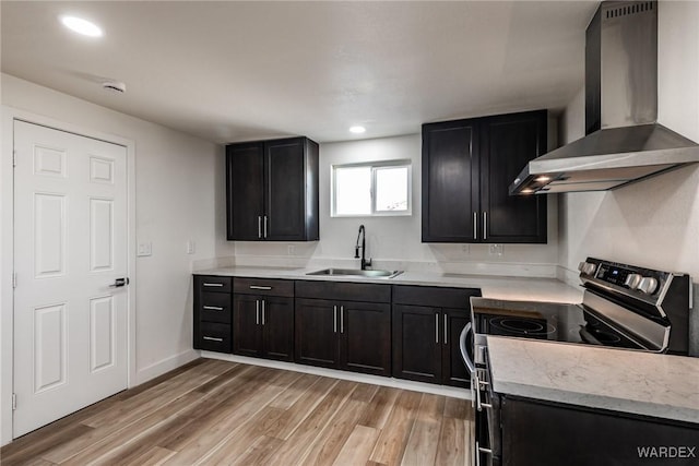 kitchen featuring light countertops, light wood-style floors, stainless steel range with electric cooktop, a sink, and wall chimney range hood