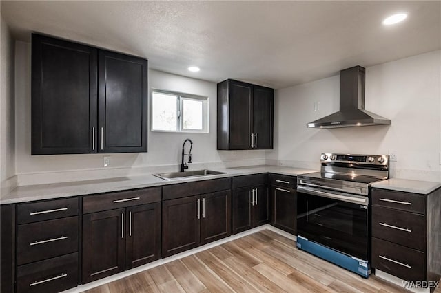 kitchen with recessed lighting, electric range, a sink, wall chimney range hood, and light wood-type flooring