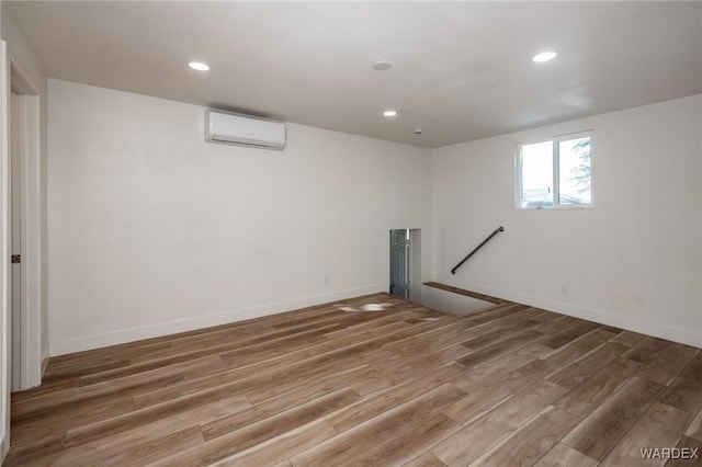 basement with recessed lighting, baseboards, an AC wall unit, and wood finished floors