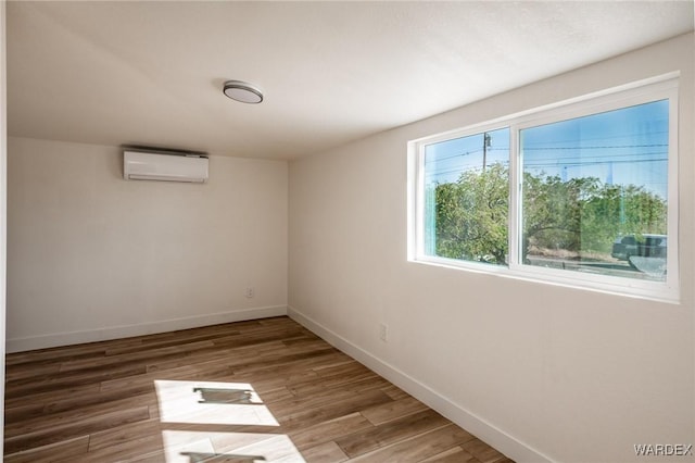 unfurnished room featuring baseboards, wood finished floors, and a wall mounted air conditioner