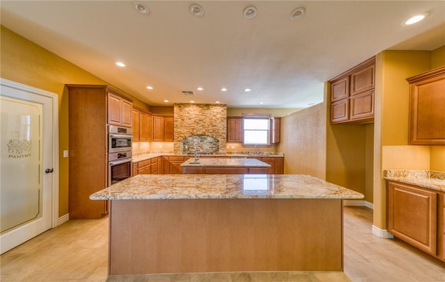 9076 E Mountain Shadow Rd, Kingman, AZ 86401 - kitchen featuring a kitchen island with sink, brown cabinets, double oven, light stone counters, and recessed lighting