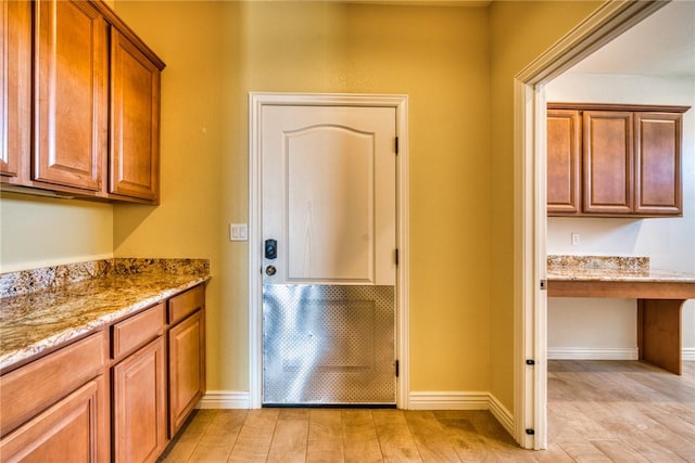9076 E Mountain Shadow Rd, Kingman, AZ 86401 - kitchen featuring light stone counters, brown cabinetry, light wood-type flooring, and baseboards