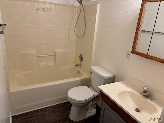 bathroom with toilet, wood finished floors, bathing tub / shower combination, a textured wall, and vanity