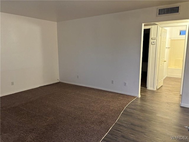 spare room featuring dark wood finished floors, baseboards, visible vents, and dark colored carpet