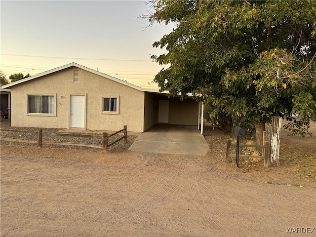 view of front of house with stucco siding, an attached carport, dirt driveway, and fence