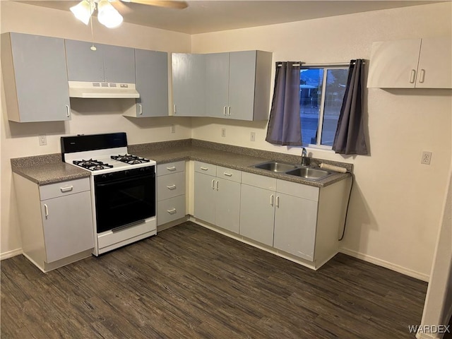 kitchen with dark countertops, a sink, under cabinet range hood, gas range, and dark wood-style flooring