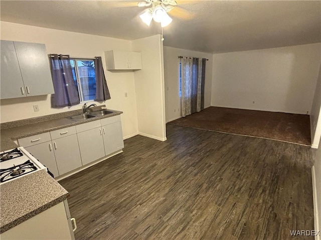 kitchen featuring dark countertops, dark wood-type flooring, ceiling fan, white cabinets, and a sink