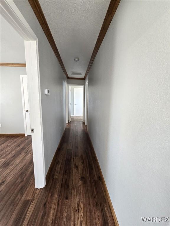 hallway with baseboards, visible vents, ornamental molding, dark wood-type flooring, and a textured ceiling