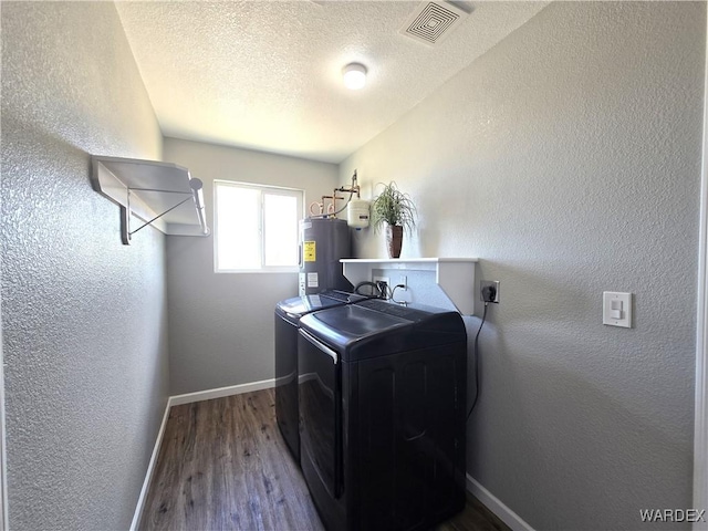 clothes washing area with laundry area, visible vents, washer and clothes dryer, a textured wall, and water heater