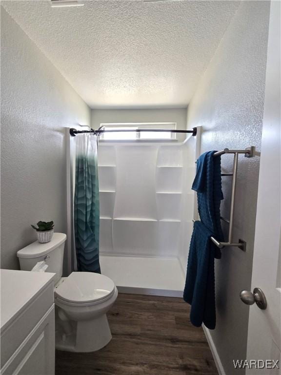 full bathroom with a textured wall, toilet, wood finished floors, vanity, and a shower stall