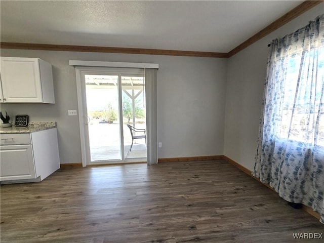 unfurnished dining area featuring baseboards, ornamental molding, and dark wood-style flooring