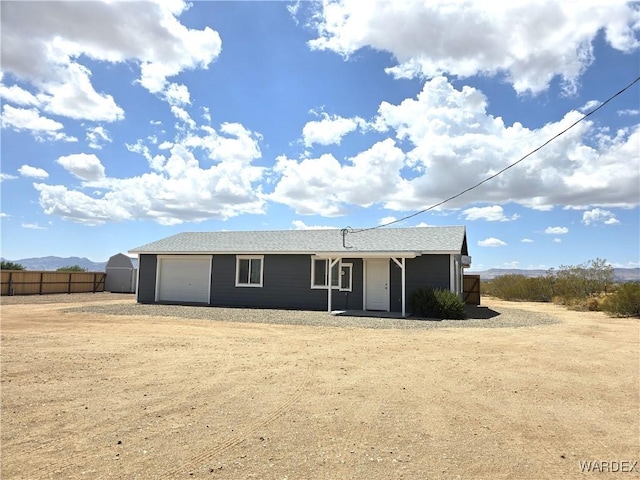 single story home with dirt driveway, an attached garage, and fence