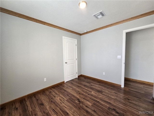 spare room featuring crown molding, dark wood-style flooring, visible vents, and baseboards