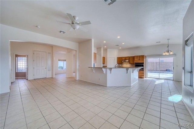 kitchen featuring light tile patterned floors, visible vents, brown cabinetry, a peninsula, and a kitchen breakfast bar