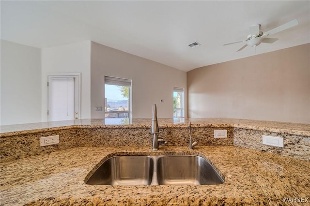 kitchen featuring ceiling fan, a sink, visible vents, and light stone countertops