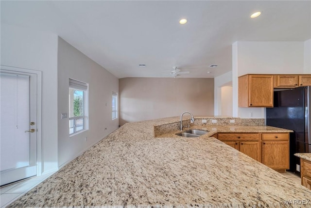 kitchen featuring light tile patterned floors, freestanding refrigerator, a peninsula, a sink, and recessed lighting