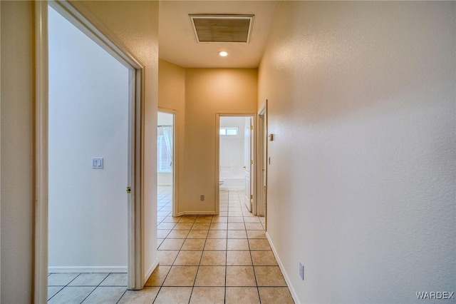 hallway with light tile patterned floors, baseboards, and visible vents