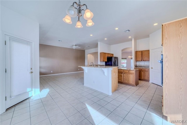 kitchen featuring arched walkways, black fridge, a center island, brown cabinetry, and decorative light fixtures