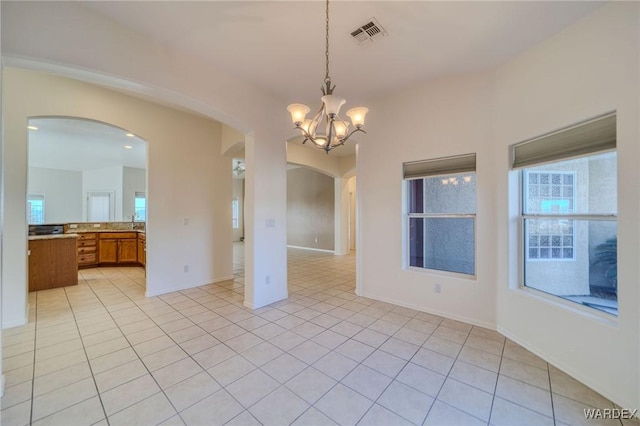 empty room with arched walkways, a notable chandelier, light tile patterned floors, visible vents, and baseboards