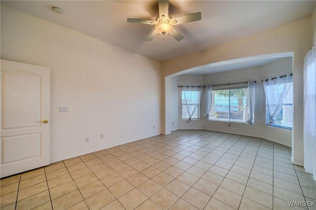 spare room featuring light tile patterned floors, baseboards, arched walkways, and a ceiling fan