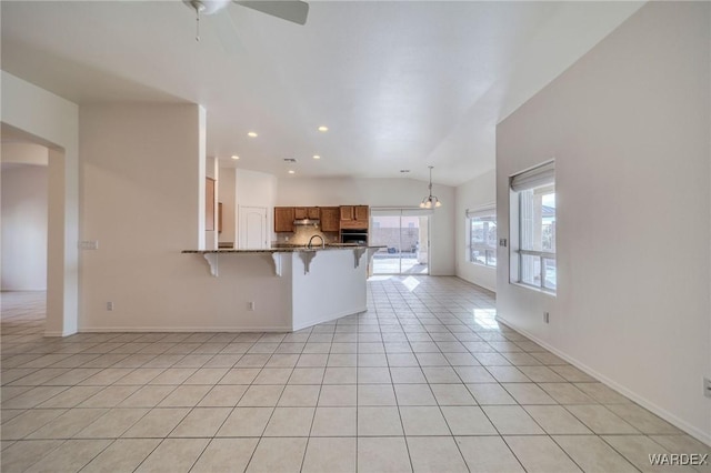 kitchen featuring brown cabinets, a breakfast bar area, light tile patterned flooring, dark stone countertops, and a peninsula