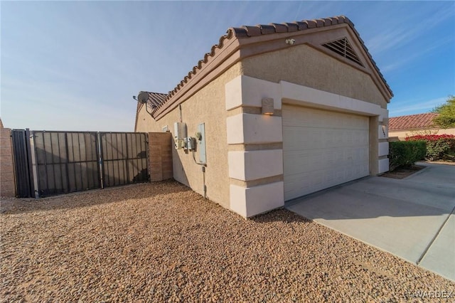 view of home's exterior featuring driveway, a garage, a tiled roof, a gate, and stucco siding