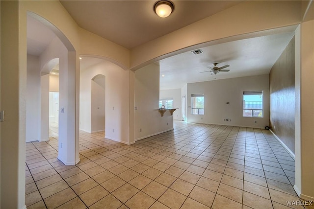 empty room featuring light tile patterned floors, visible vents, arched walkways, baseboards, and ceiling fan