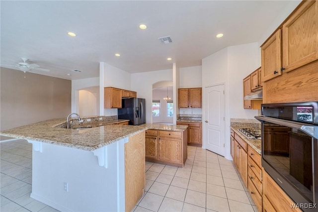 kitchen with arched walkways, a peninsula, under cabinet range hood, black appliances, and a kitchen bar